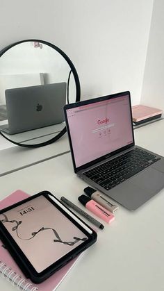 an open laptop computer sitting on top of a white desk next to a pink notebook