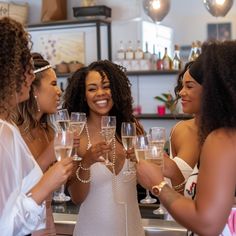 three women are holding wine glasses and smiling at each other while standing in front of a bar