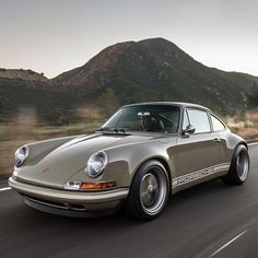 a silver porsche sits on the road in front of mountains