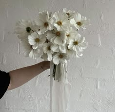 a person holding a vase with white flowers in it