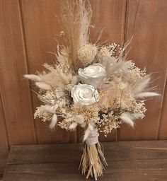 a bridal bouquet with white roses and feathers on a wooden table in front of a wood paneled wall