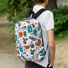 A boy faced with back to camera and a backpack on his shoulders. The backpack has a white background with a basketball themed pattern backpack featuring illustrated basketballs, basketball jerseys, whistles, referee shirts, basketball hoops, stars, basketball shoes, fun play sketches and the word swish. The backpack straps are black. Casual Backpack For Sports Events, Casual College Backpack, Sporty Backpack For Sports And End Of School Year, Sporty Backpack With Zipper Closure, Blue Sports Backpack With Zipper Closure, Basketball Purse, Referee Shirts, Sporty On-the-go Backpack With Adjustable Strap, Basketball Backpack