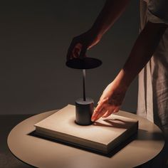 a person standing over a book on top of a table with a candle in it