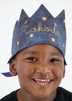 a young boy wearing a blue crown hat with gold lettering on the front and sides