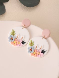 two white earrings with flowers on them sitting on top of a table next to a potted plant