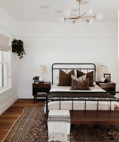 a bedroom with white walls and wood flooring has a black iron bed frame, two nightstands, and a rug on the floor