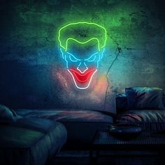 a neon joker mask is lit up on the wall above a couch in a dark room