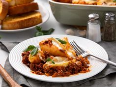 a white plate topped with lasagna covered in sauce and cheese next to bread