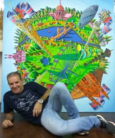 a man laying on the floor in front of a large painting with buildings and flags