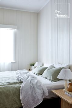 a bed with white sheets and green pillows in a small room next to a window