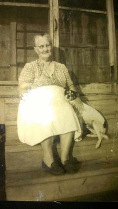 an old black and white photo of a woman sitting on the porch with her dog