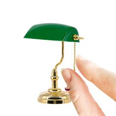 a hand holding a green desk lamp on top of a white surface with a gold base