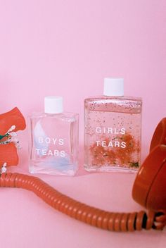 two perfume bottles and an old telephone on a pink background with the words boys tears written on them