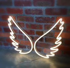 a neon angel wings sign on a brick wall