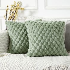 two green pillows sitting on top of a bed next to a vase filled with flowers