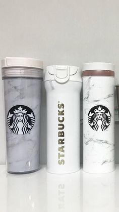 three starbucks cups lined up next to each other on a white counter top with the words starbucks printed on them