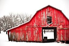 an old red barn with snow on the ground