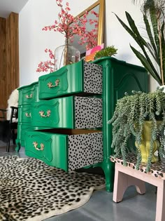 a green dresser with leopard print on the drawers next to a pink stool and potted plant