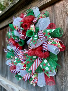 a christmas wreath hanging on the side of a wooden fence with red, green and white ribbons