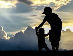 a man holding the hand of a child in front of a cloudy sky at sunset