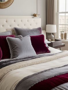 a bedroom with a large bed covered in red and grey pillows next to a window