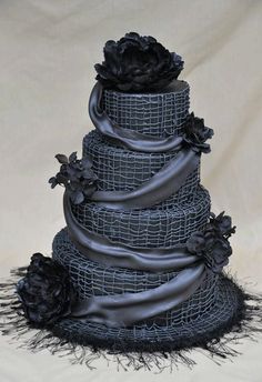 a three tiered cake with black frosting and flowers on the top is covered in netting