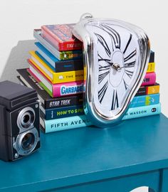 a clock sitting on top of a stack of books next to a pile of books