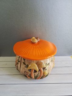 an orange lidded container sitting on top of a white wooden table next to a gray wall