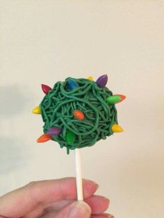 a hand holding a lollipop with green noodles and colorful lights on it's top