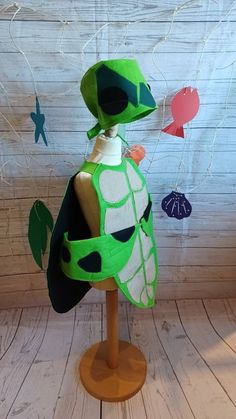 a green and white stuffed animal sitting on top of a wooden table next to a wall