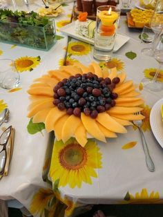 a sunflower centerpiece with grapes and blueberries sits on a table set for an outdoor dinner