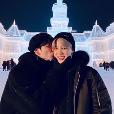 two people standing next to each other in front of a building with snow on it