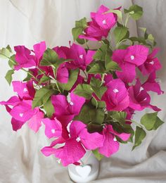 a white vase filled with pink flowers and green leaves