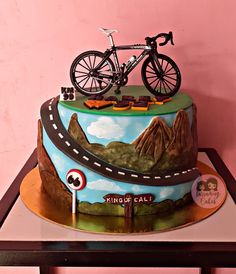 a cake decorated with a bike on top of a hill and road sign that says king's call