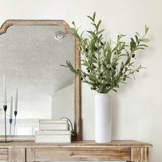 a white vase sitting on top of a wooden table next to a mirror and books