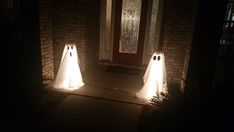 three white ghost statues in front of a door at night with lights shining on them