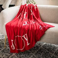 a red blanket with the word joy on it is sitting on a chair in front of a white couch