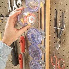 a person holding a container in front of a pegboard with various tools on it