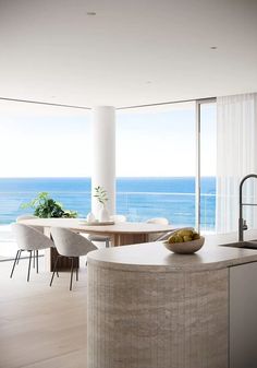 a modern kitchen with an ocean view is pictured in this image, while the dining room table and chairs are also visible