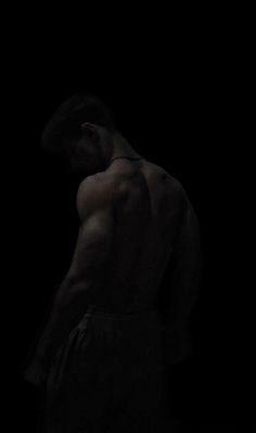 a shirtless man standing in the dark with his hands on his hips looking down