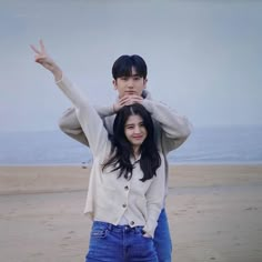 a man and woman standing on top of each other in front of the ocean holding their hands up