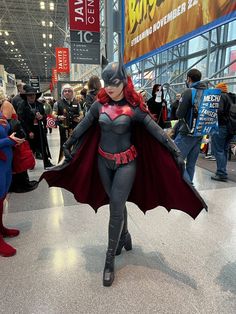 a woman dressed as batgirl walking through a convention hall with other people in the background