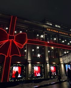 people are walking in front of a building decorated with christmas lights and large red bow