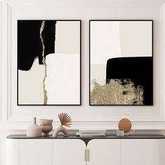 two black and white paintings hanging on the wall next to a table with vases