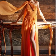 a woman in an orange dress standing next to a table with a long scarf on it