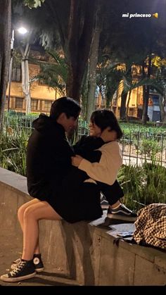 a man and woman sitting on top of a cement wall next to each other at night