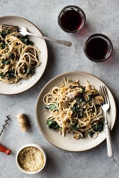 two plates of pasta with mushrooms and broccoli next to a glass of wine