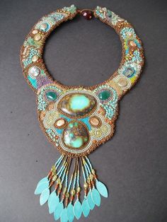 an elaborate necklace with beads and feathers on a gray surface, featuring turquoise stones in the center