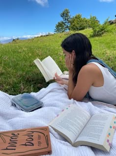 a woman laying on top of a blanket reading a book next to an open book