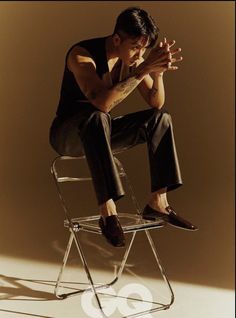 a man sitting on top of a chair with his hands clasped to his chest and legs crossed